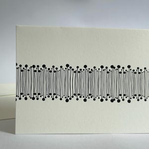 May include: A cream-colored greeting card with a black, abstract design. The design features vertical lines with small circles at the top and bottom, creating a unique pattern. An envelope is visible in the background. Stationery.