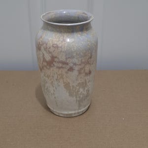 May include: A ceramic vase with a wide, rounded body and a flared rim. The surface features a mottled glaze with blended tones of pale blue, soft beige, and creamy white, creating an organic, textured appearance across the entire exterior.