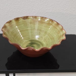 May include: A ceramic bowl with a ruffled, scalloped rim. The interior features a light, glossy lime green glaze with visible brushstroke textures, while the exterior and the edge of the rim are finished in a solid, smooth, deep reddish-brown glaze.