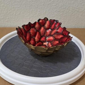 May include: A small, decorative bowl with a deep red, honeycomb-patterned interior and a metallic gold exterior. The rim of the bowl has an irregular, organic shape, and the interior surface features a glossy, textured finish with raised cells.