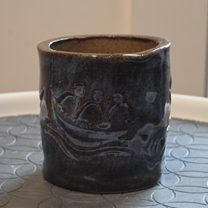 Taza de cerámica artesanal firmada a mano con relieve figurativo y escena de barco con esmalte azul de goteo.