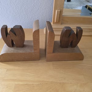 May include: A pair of wooden bookends. Each bookend has a rectangular base and a vertical support. The letters "W" are carved into the front of each bookend. The wood has a natural finish.