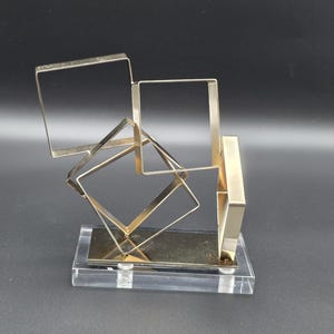 Escultura cúbica de metal tono dorado con base de lucita, modernista, 20 cm, finales del siglo XX.
