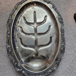May include: Oval silver-plated serving platter with an ornate border. The interior has a raised, tree-like design for holding food. The platter shows signs of age and use, adding to its vintage appeal.