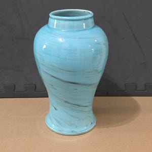 Könnte beinhalten: Eine hellblaue Keramikvase mit glänzender Oberfläche und dunkelgrauen, wirbelnden, marmorartigen Mustern auf dem gesamten Körper. Die Vase hat einen breiten, abgerundeten Mittelteil, der sich zu einer schmalen Basis hin verjüngt.