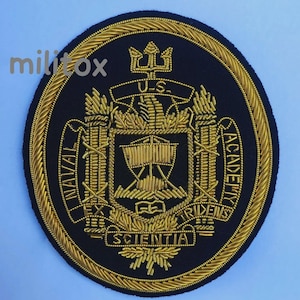 Op de afbeelding: Een marineblauwe patch met goud geborduurde details. De patch toont de woorden "U.S. Naval Academy" en "Scientia Tridens" rond een centraal embleem van een schip en een drietand. Een gouden rand omlijst het ontwerp.