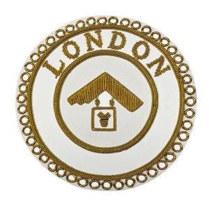 Puede incluir: Un objeto decorativo circular blanco con bordado dorado. La palabra "LONDON" está bordada en oro en la parte superior. Un ala delta y un letrero dorados están en el centro. El borde exterior está adornado con círculos dorados.