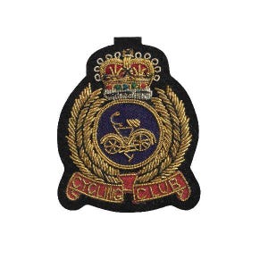 Op de afbeelding: Geborduurde patch met een fiets in een blauwe cirkel, omringd door goudkleurige tarwearen. Boven de cirkel staat een kroon en de woorden "CYCLING CLUB" staan op een rode banner. De patch heeft een zwarte rand.