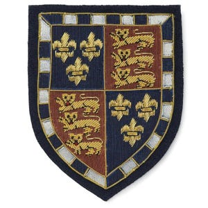 May include: Embroidered shield patch with a navy blue border. The shield is divided into quadrants of navy blue and maroon, featuring gold fleur-de-lis and lions. The border has silver and gold accents.