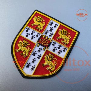 Op de afbeelding: Geborduurde schildvormige patch met een heraldisch ontwerp. De patch heeft een rood, wit en goud kleurenschema, met leeuwen en andere symbolen. De tekst "militox since 1999" is zichtbaar. Met gouden rand.