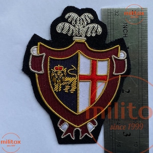 Puede incluir: Parche bordado con forma de escudo con diseño de escudo de armas. El parche presenta un león, una cruz y elementos decorativos en oro, rojo, blanco y azul marino. El parche mide aproximadamente 7,6 cm de altura.