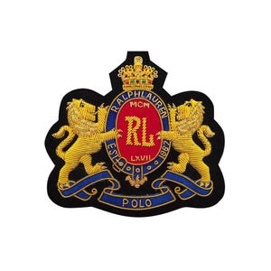 May include: Embroidered patch with a crest design. Two golden lions flank a central oval with "RL" and the words "RALPH LAUREN MCM LXVII 1967". A blue ribbon at the bottom reads "POLO". The patch is black with gold, red, and blue details.