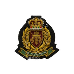 Op de afbeelding: Geborduurde patch met een koninklijk wapenontwerp. De patch heeft een zwarte achtergrond met gouden borduursel dat een kroon, schild en laurierbladeren voorstelt. Onderaan een groene banner met witte sterren.