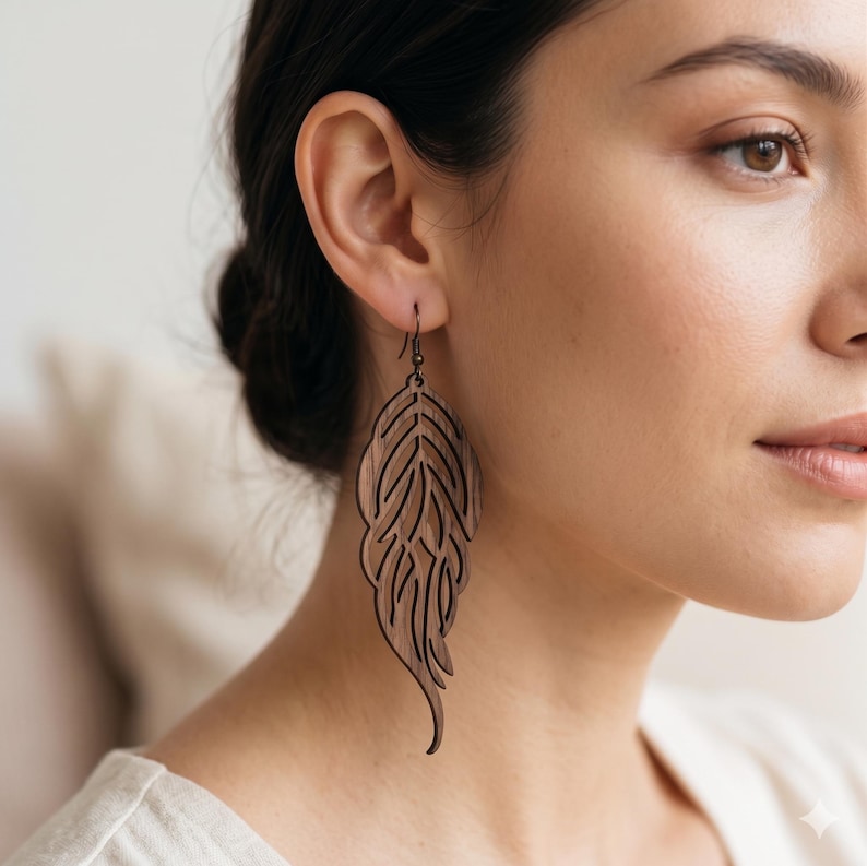 May include: A dark brown wooden dangle earring featuring a laser-cut feather or leaf design with intricate internal cutouts. The earring hangs from a thin, dark metal hook, showcasing a natural wood grain texture and a long, slender, curved shape.