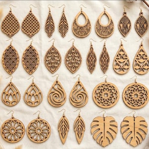 May include: A collection of twenty-eight wooden earrings arranged in fourteen pairs. The earrings feature various laser-cut designs including teardrop, circular, and leaf shapes with intricate geometric, floral, and swirling patterns.