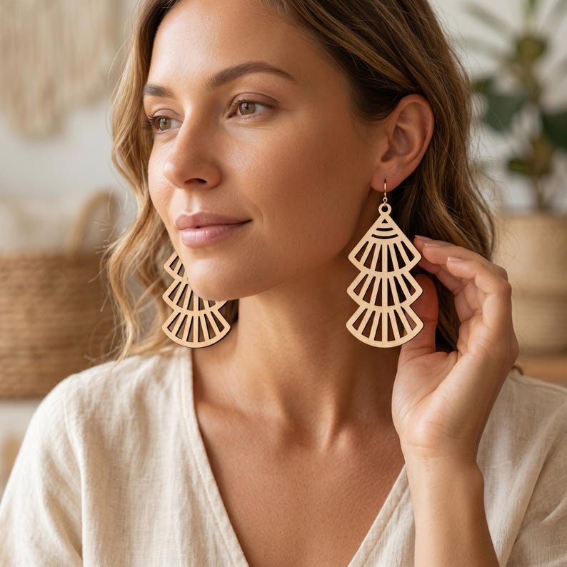 May include: A pair of light-colored wooden earrings featuring a tiered, fan-shaped design with vertical cutouts. Each earring consists of three stacked, semi-circular segments that decrease in width toward the top, suspended from a small metal hook.