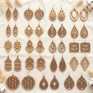 May include: A collection of twenty-five pairs of light brown wooden laser-cut earrings arranged in a grid. The earrings feature various geometric, floral, leaf, and mandala-inspired patterns with intricate cutouts, all suspended from metal earring hooks.