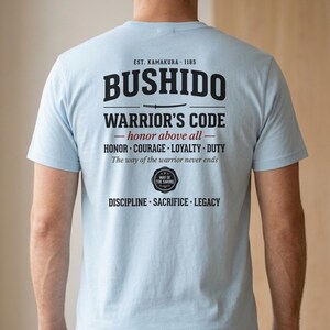 May include: A light blue t-shirt featuring black and red text on the back. The design includes the words BUSHIDO, WARRIOR'S CODE, honor above all, HONOR, COURAGE, LOYALTY, DUTY, The way of the warrior never ends, DISCIPLINE, SACRIFICE, LEGACY.