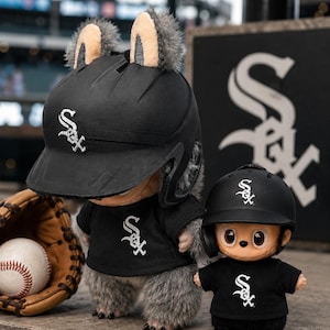 Puede incluir: Dos figuras de peluche con cascos y camisetas de b&eacute;isbol negros con el logo "SOX". Una figura tiene orejas peludas. Tambi&eacute;n hay una pelota de b&eacute;isbol, un guante y un bate.