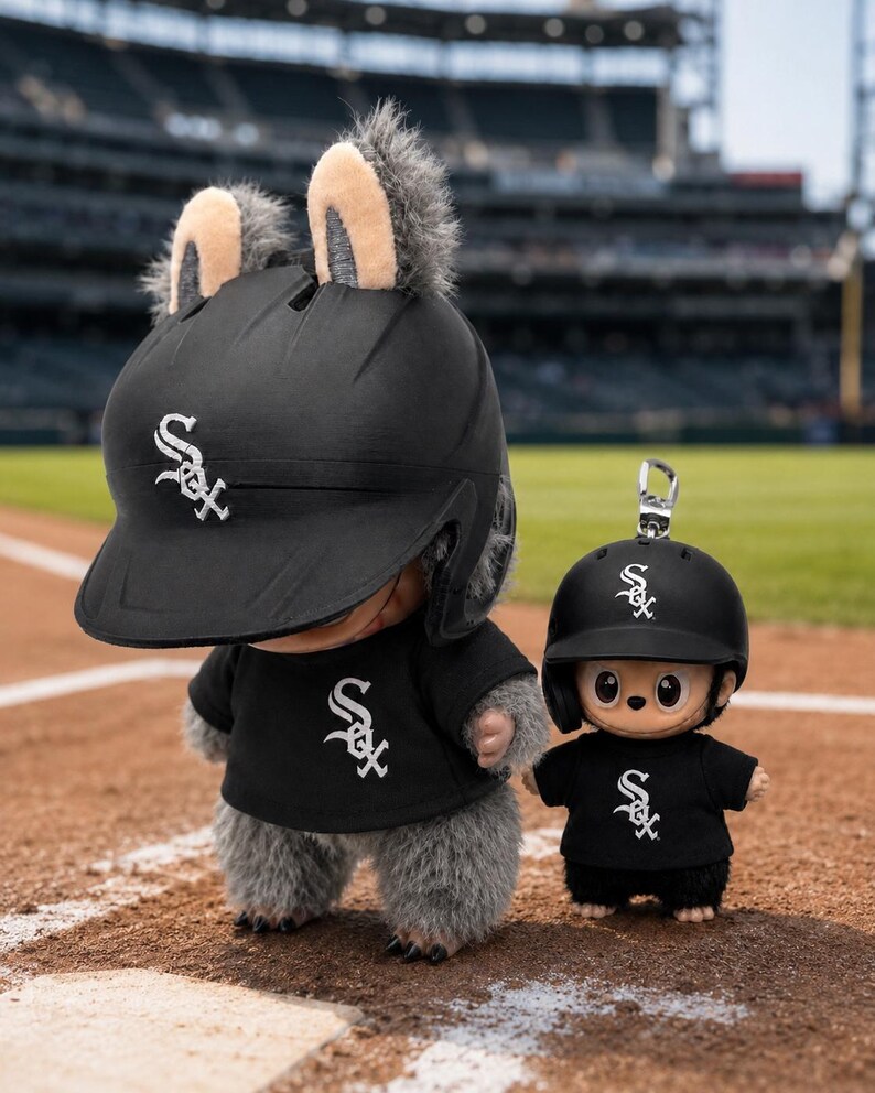 Puede incluir: Dos figuras de peluche con cascos y camisetas de b&eacute;isbol negros con el logotipo de los White Sox de Chicago. La figura m&aacute;s grande tiene orejas peludas en el casco. Est&aacute;n en un campo de b&eacute;isbol.