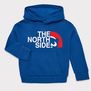 May include: A blue hoodie with a kangaroo pocket and a hood. The front features the text "THE NORTH SIDE" in white, with a red and white graphic. The hoodie is made of a soft material.