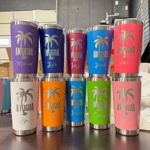 May include: A collection of insulated tumblers in various colors, including purple, blue, red, and pink. Each tumbler features a silver palm tree design and the word "Antigua" with a name below. The tumblers are stainless steel and have a silver rim.