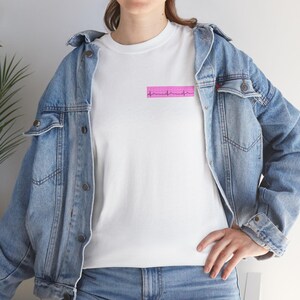 Peut inclure: T-shirt blanc avec un motif rectangulaire rose représentant une ligne de battement de cœur. Le t-shirt est porté avec une veste en jean bleu clair.