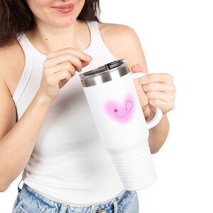 Peut inclure: Mug de voyage blanc avec un cœur rose et un motif de stéthoscope. Le mug a un couvercle argenté et une poignée. Une paille transparente est insérée dans le couvercle. Le mug est conçu pour garder les boissons chaudes ou froides.