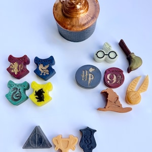 May include: A collection of small, molded wax or resin figures featuring iconic shapes including a brown sorting hat container, four house crests, round tokens with HP and 9 3/4 text, glasses, a broom, a golden snitch, a triangle, and a goblet.