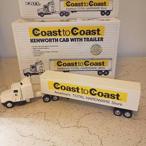 May include: A white die-cast metal Kenworth semi-truck toy with a trailer featuring the yellow and black Coast to Coast America's TOTAL HARDWARE Store logo. The toy is displayed in front of its original white cardboard packaging box.