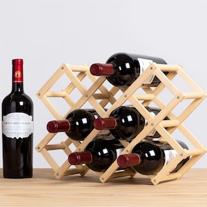 May include: A wooden wine rack holding six bottles of red wine, with a seventh bottle standing upright to the left. The rack is made of light-colored wood and has a diamond-shaped design. The wine bottles are dark with red foil.