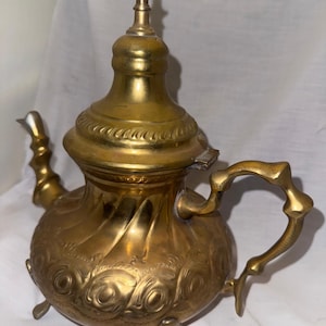 Peut inclure: Une théière vintage en laiton avec un design décoratif. La théière a une poignée incurvée, un bec verseur et un couvercle avec un fleuron. Le corps de la théière est orné de motifs floraux en relief et repose sur trois petits pieds.