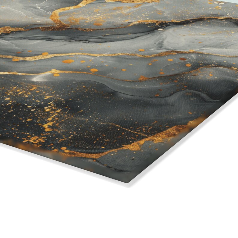 May include: A rectangular wall art panel featuring an abstract fluid ink design. The surface displays swirling layers of charcoal gray, slate, and black tones, accented by prominent, flowing veins and scattered droplets of metallic gold paint.