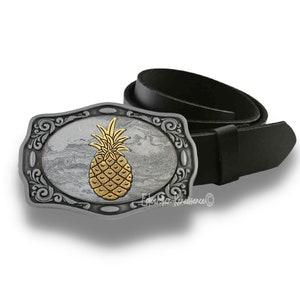 May include: A silver belt buckle with an ornate design features a gold pineapple on a gray marble background.