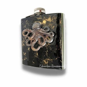 May include: A stainless steel hip flask with a black and gold marbled pattern. It features a silver octopus emblem. The flask has a silver cap and edge. The text "Edwardian Renaissance" is printed on the bottom right.