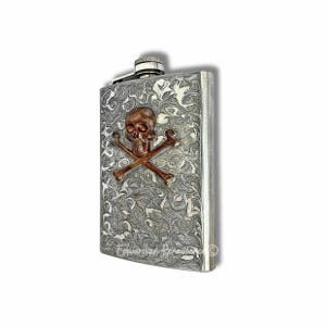 May include: A silver flask with a decorative pattern and a copper-colored skull and crossbones emblem. The flask has a hinged cap and a polished finish, perfect for carrying spirits. The flask is rectangular in shape.