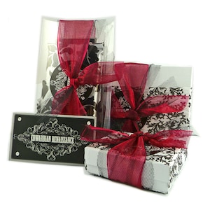 May include: A gift box wrapped in white paper with a black and white damask pattern. The box is tied with a red satin ribbon and topped with a black and white tulle bow. The box is sitting on a white surface. The box is labeled "Edwardian Renaissance".