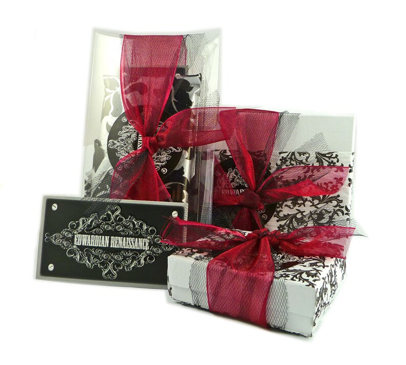 May include: A gift box wrapped in white paper with a black and white damask pattern. The box is tied with a red satin ribbon and topped with a black and white tulle bow. The box is sitting on a white surface. The box is labeled "Edwardian Renaissance".