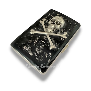 Caja de cigarrillos de calavera plateada y tibias cruzadas con incrustaciones en diseño de remolino de tinta negra brillante pintada a mano con opción personalizada y de color