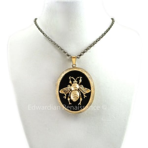 May include: A gold locket necklace with a black oval cameo featuring a gold bee design. The chain is silver.