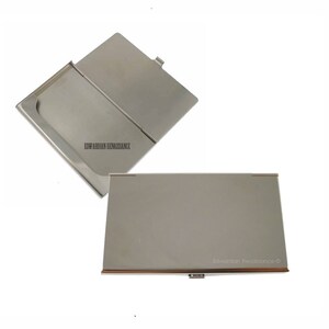 May include: A silver metal business card holder with a hinged lid. The holder is closed in the first image and open in the second image. The text "Edwardian Renaissance" is engraved on the holder.
