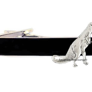 May include: A silver tie bar with a black enamel bar and a silver Tyrannosaurus Rex figurine.