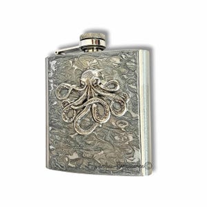 Puede incluir: Un petaca de acero inoxidable con un diseño detallado de pulpo. La petaca tiene un patrón veteado texturizado y una tapa plateada. El pulpo está en relieve y tiene detalles intrincados.