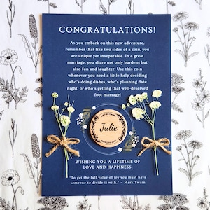 May include: A navy blue wedding card with the text "CONGRATULATIONS!". It features a wooden coin with the name "Julie" and sprigs of white flowers tied with twine. The card includes a quote by Mark Twain.