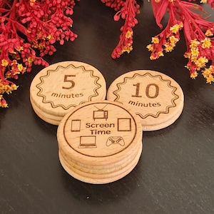 May include: Wooden screen time tokens with engraved text and icons. The tokens are round with a scalloped edge. One token reads "5 minutes", another "10 minutes", and a third says "Screen Time" with icons of a TV, tablet, laptop, and game controller.
