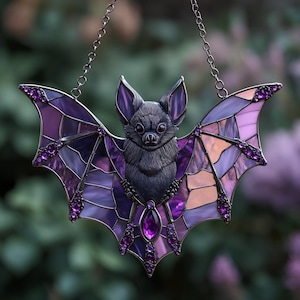 May include: A decorative bat-shaped suncatcher with a detailed, dark grey bat body and stained glass wings. The wings feature shades of purple and pink, with a chain for hanging and purple gem accents.