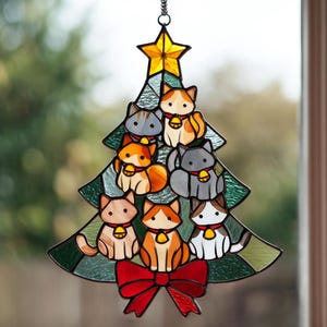 May include: Stained glass Christmas tree decoration featuring cartoon cats. The tree is green with a yellow star on top and a red bow at the bottom. Each cat has a bell collar. The cats are various colors.