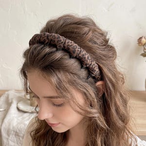 May include: A brown and black leopard print headband worn in the hair. The headband is made of a soft, padded material. The hair is long and wavy, with a natural color. The headband is a stylish hair accessory.