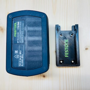 Könnte beinhalten: Ein schwarzer und grüner Festool Li-Ion-Akku und ein schwarzer Batteriehalter. Der Akku trägt die Aufschrift "FESTOOL" und "BP 18 Li 5,2 ASI". Der Halter hat ebenfalls das "FESTOOL"-Logo.