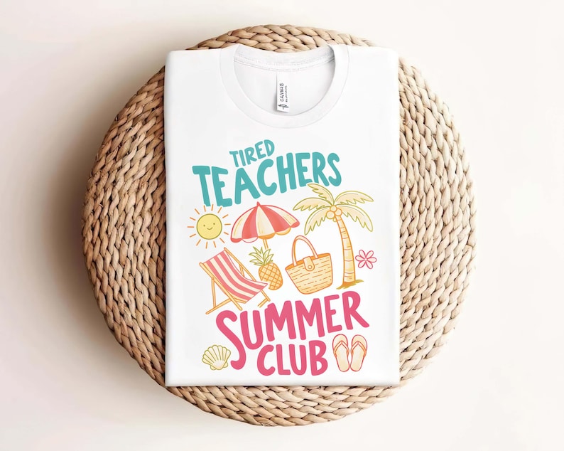 May include: White t-shirt with the text "Tired Teachers Summer Club" in teal and pink. The graphic includes a sun, beach umbrella, palm tree, beach chair, pineapple, and flip-flops. The shirt is folded on a woven surface.